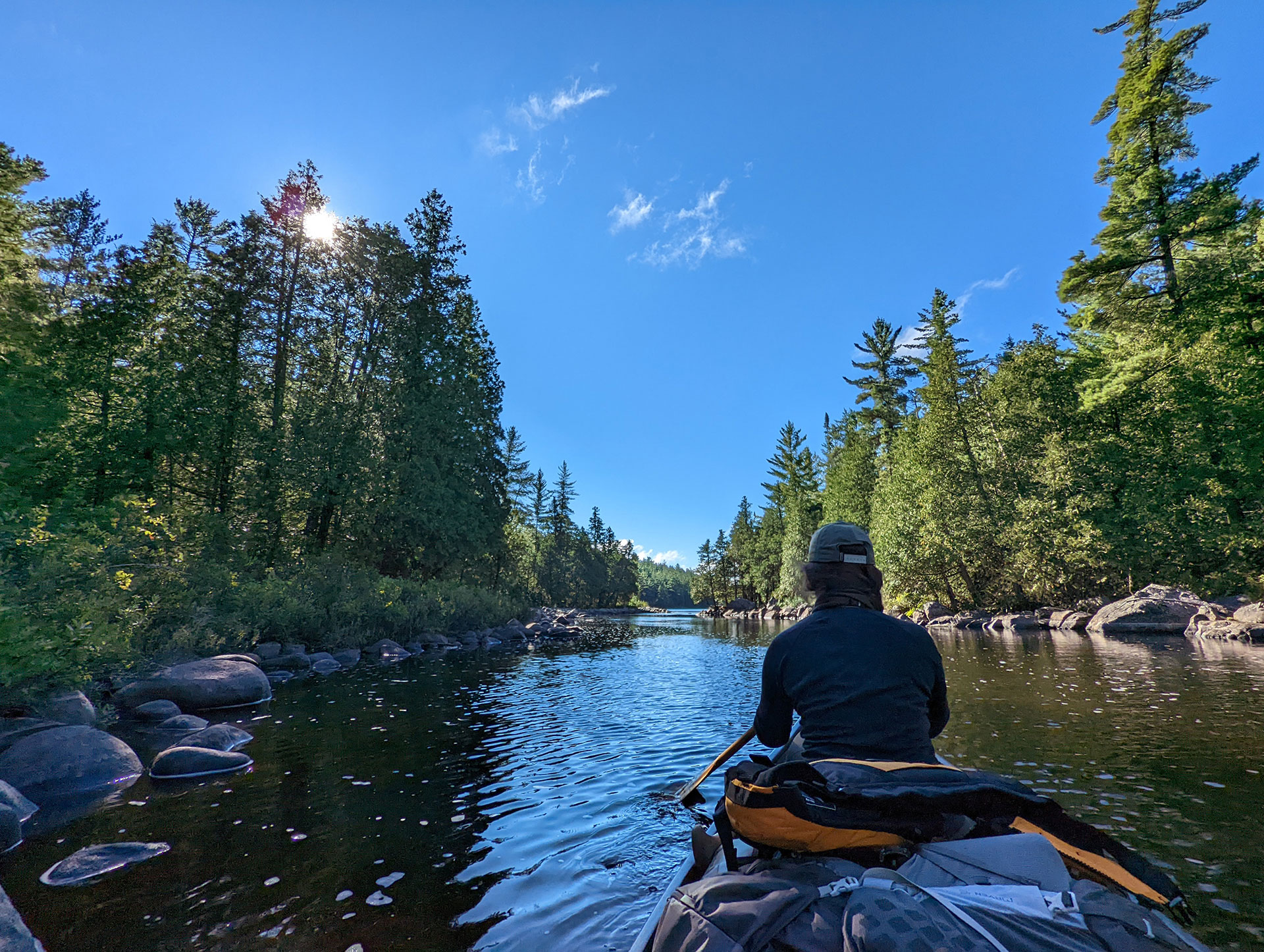 person paddles a canoe down a river in Temagami
