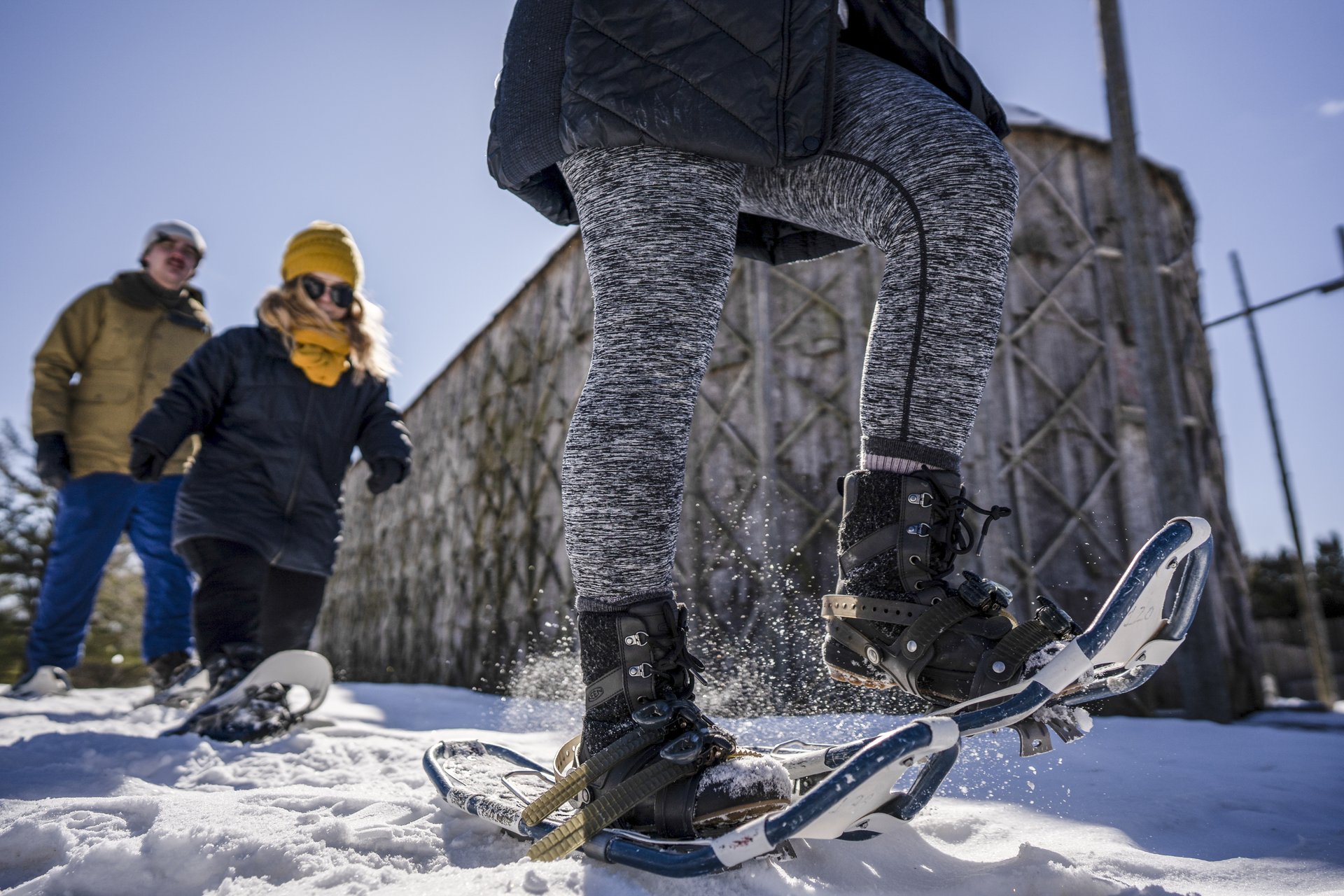 three people snowshoeing in front of a longhouse