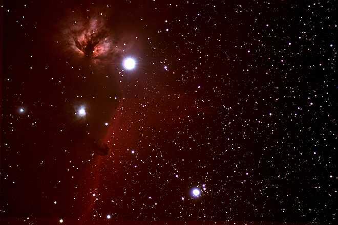 Flame and Horsehead Nebulas; 3 very large, bright white stars surrounded by a red haze and the blackness of space, dotted with many smaller stars.