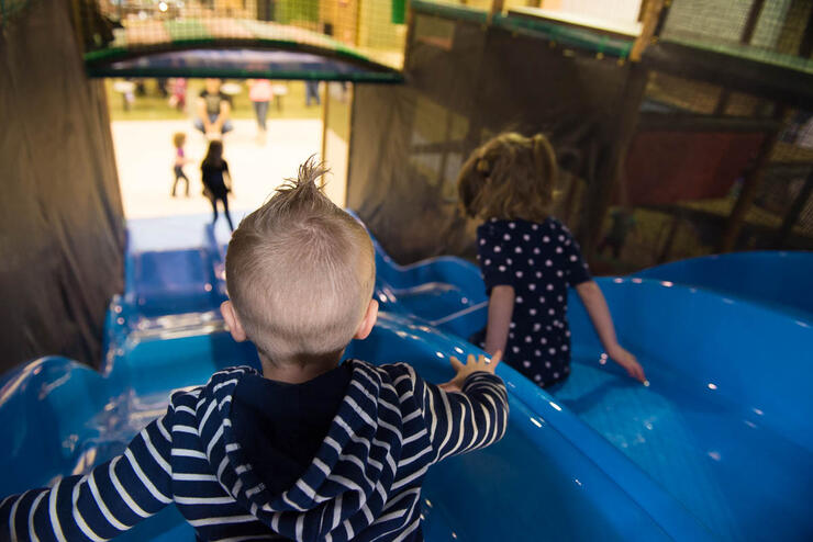 2 children sit a the top of 2 very tall indoor slides at Maple Tops indoor playground.