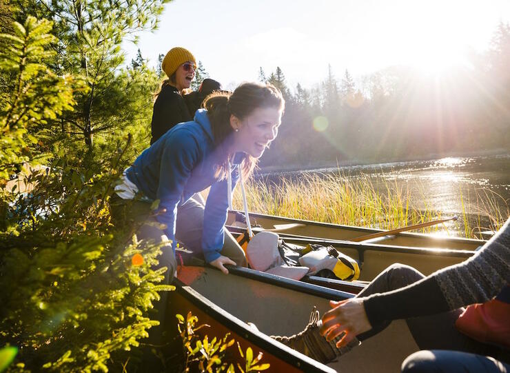 Woman holding the front of a canoe on shore. 