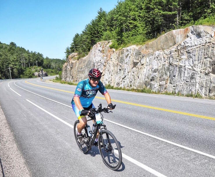 Man cycling on the paved shoulder of a highway.