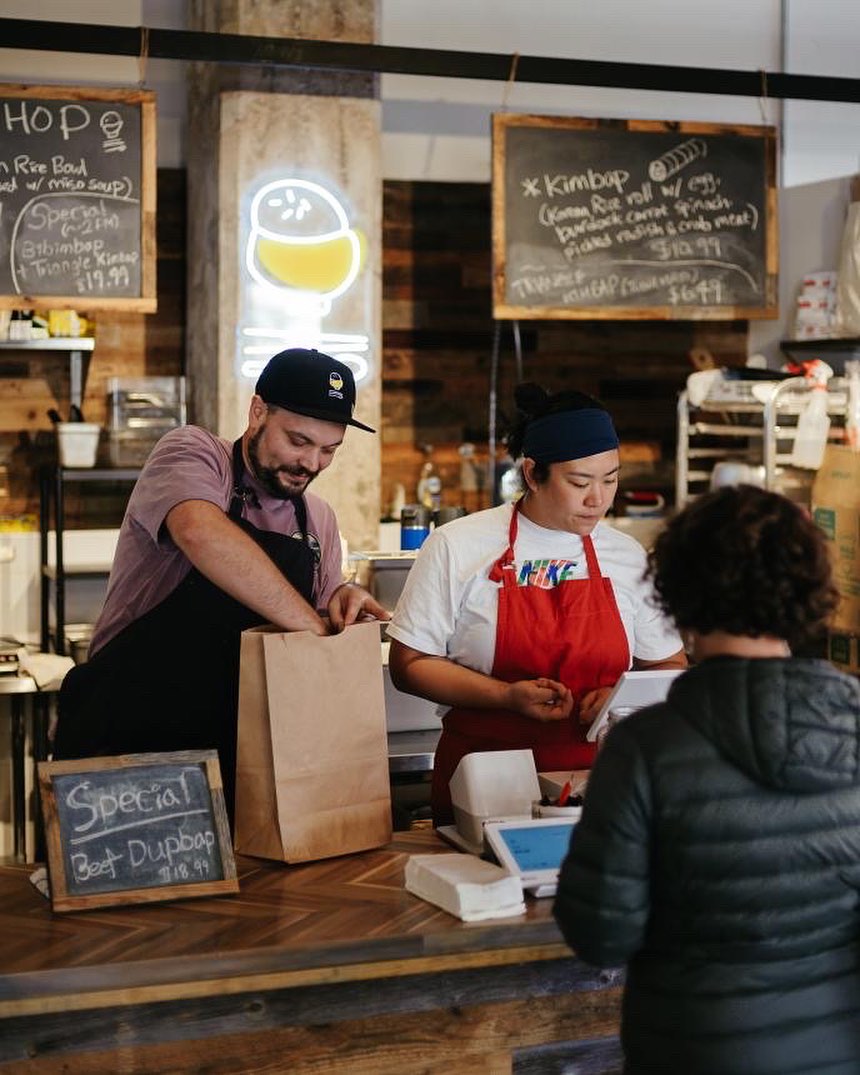 Two workers wearing aprons serving food at a restaurant.