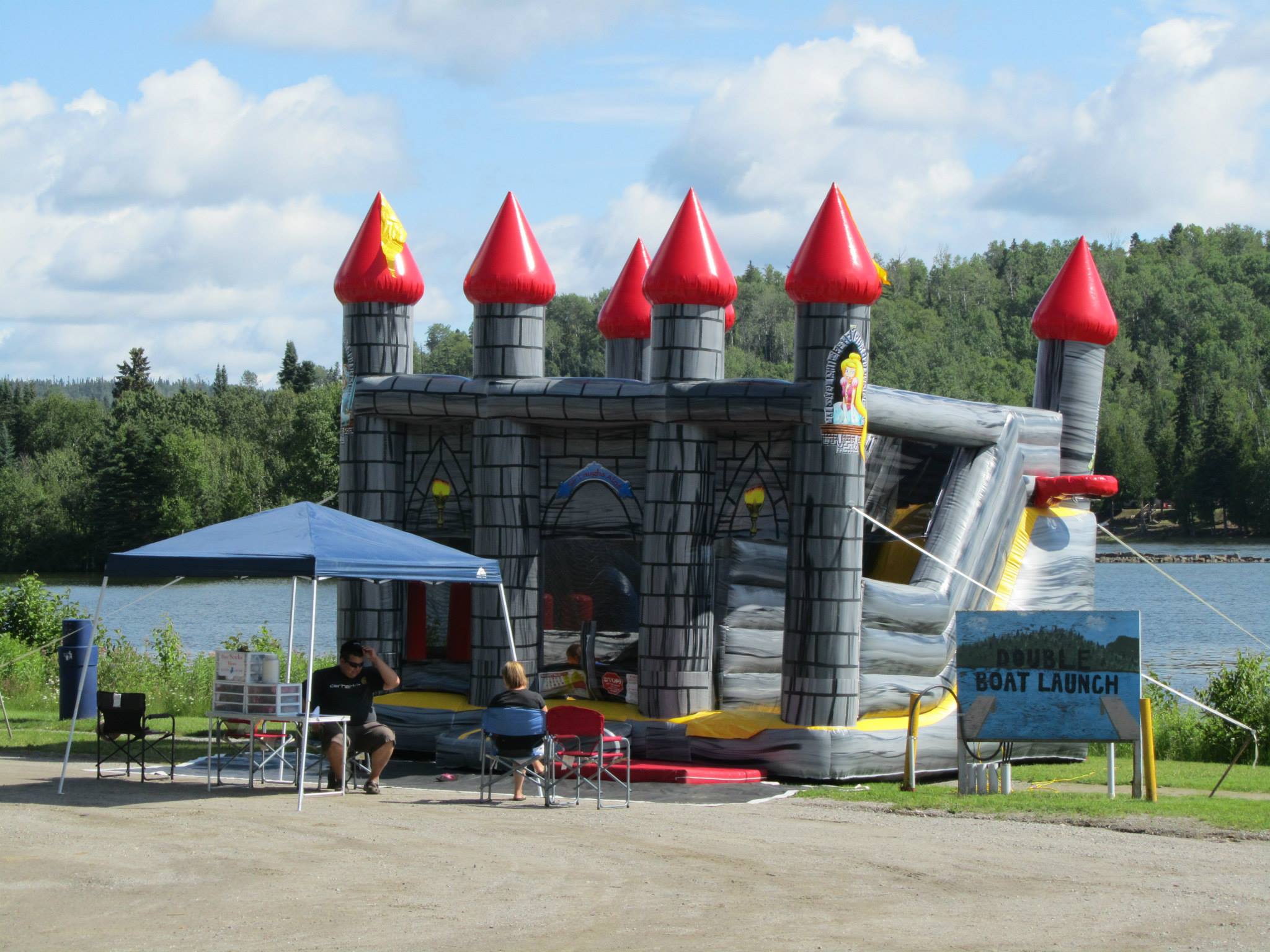 A large inflatable bouncy castle next to a blue lagoon surrounded by forest at the Nipigon Blueberry Blast Festival