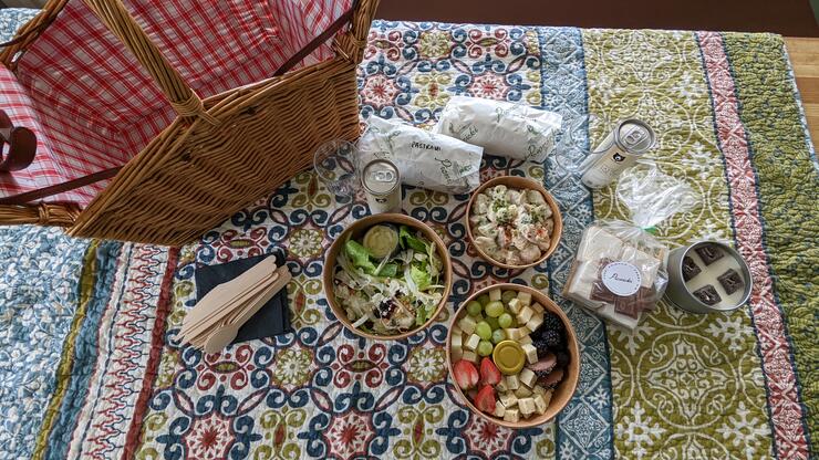A delicious-looking picnic laid on a patterned blanket next to a wicker basket.