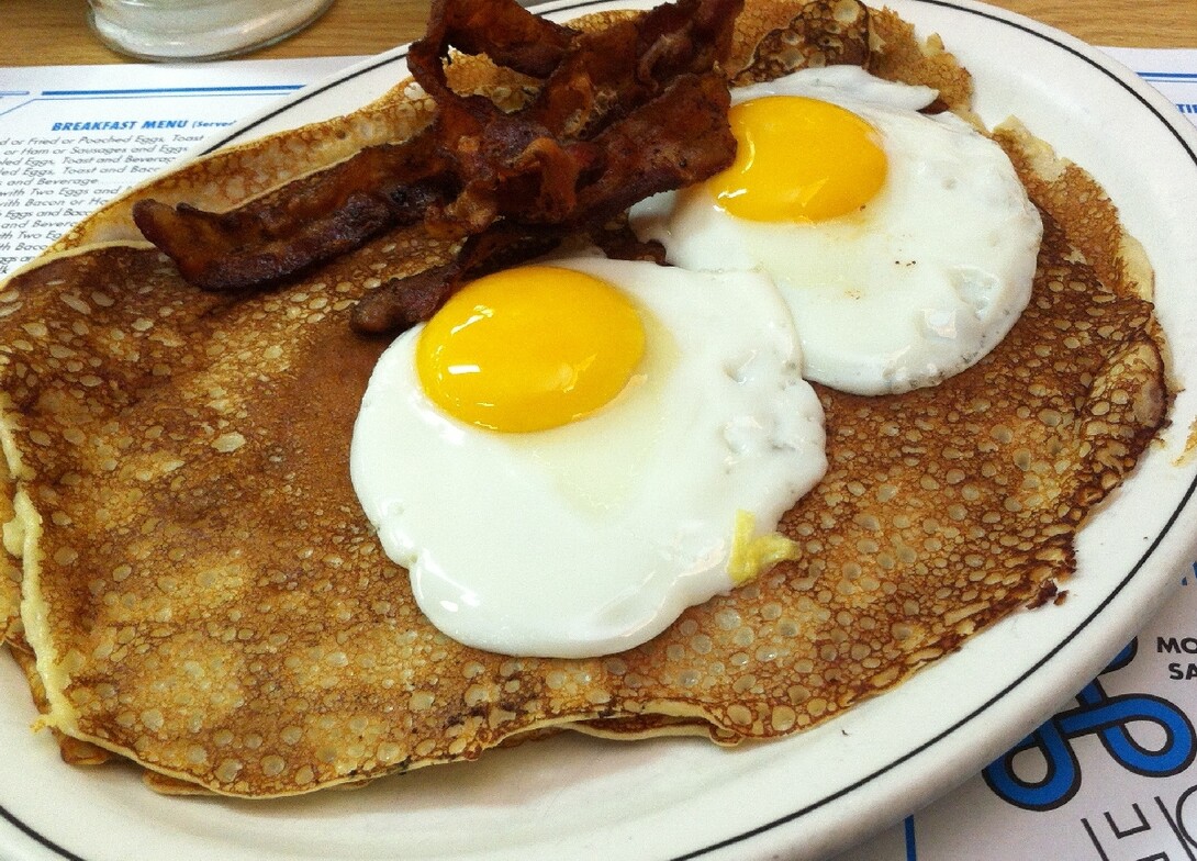 A plate of finnish pancakes and sunny-side up eggs with bacon