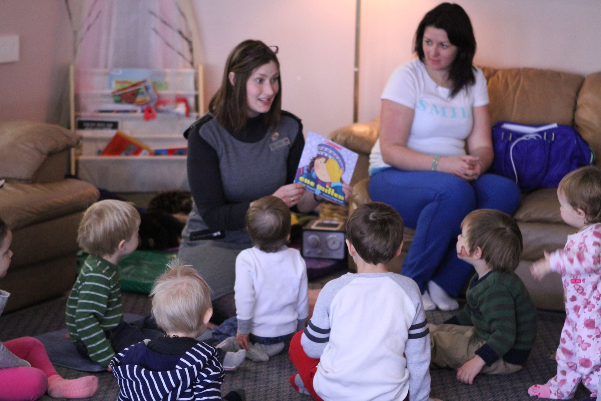 a woman looks happy and animated as she reads a story to a circle of small children. 