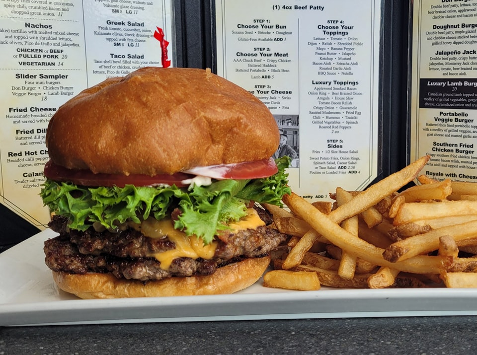 A very thick burger with lettuce, cheese, and tomato with a side of fries next to the Burger Don menu.