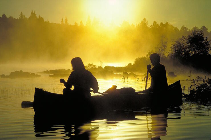 Two people in a canoe in the early morning misty sunrise.