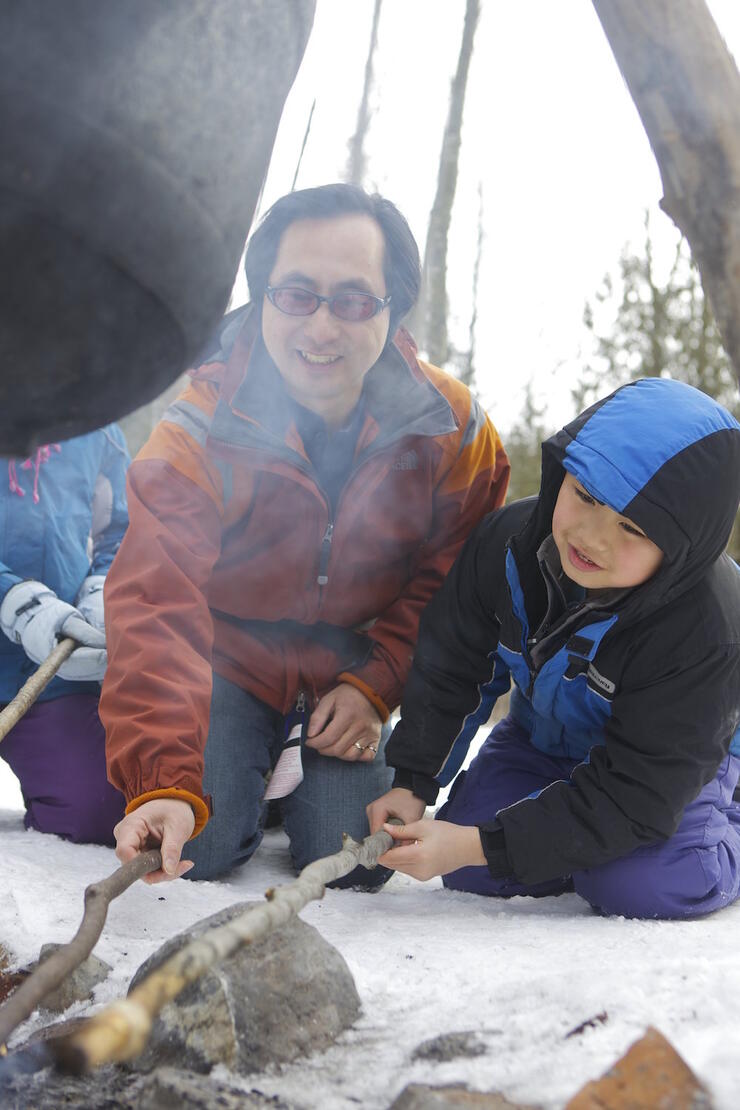 Man and son cooking bannock over fire. 