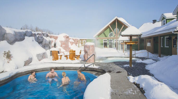 People in a hot pool in winter beside a resort.