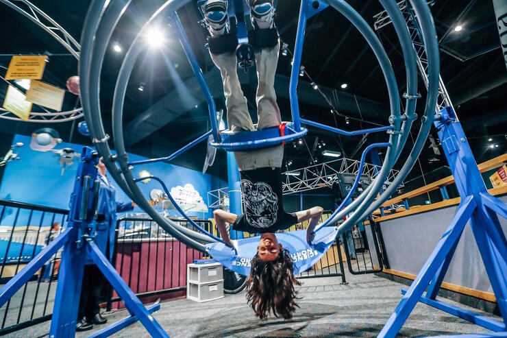 A girl hanging upside down in a contraption at Science North.