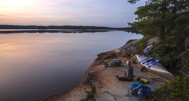 Woman sitting on a smooth rock shoreline watching sunset. 