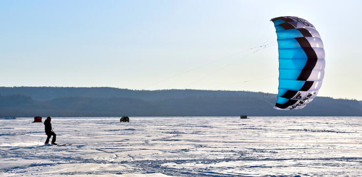 Person snowkiting on a lake with fish huts.