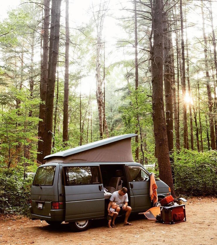 Camper van with pop-up top parked in a forest.