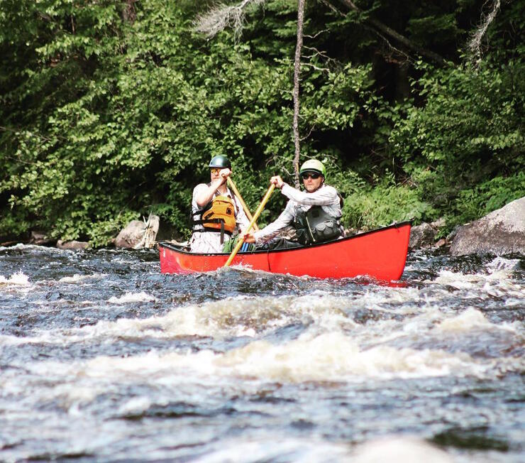 Two people paddling a red canoe in whitewater.