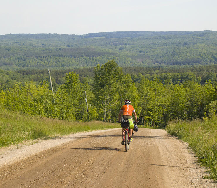 Cyclist riding on a gravel road, about to go down a big hill.