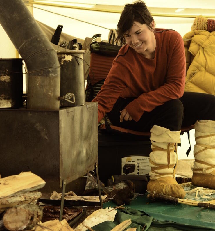 Woman beside small wood stove inside canvas tent