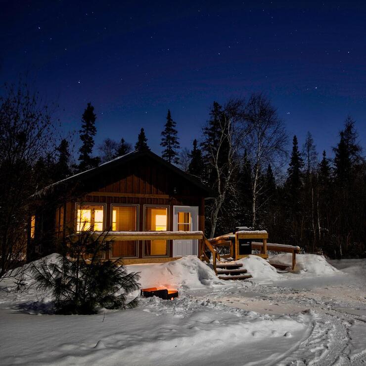 Cozy wooden cabin surrounded by snow, with lights glowing in windows.
