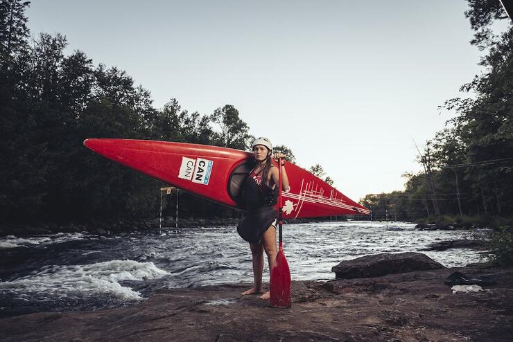 Woman standing on rocks with river in behind, holding a kayak