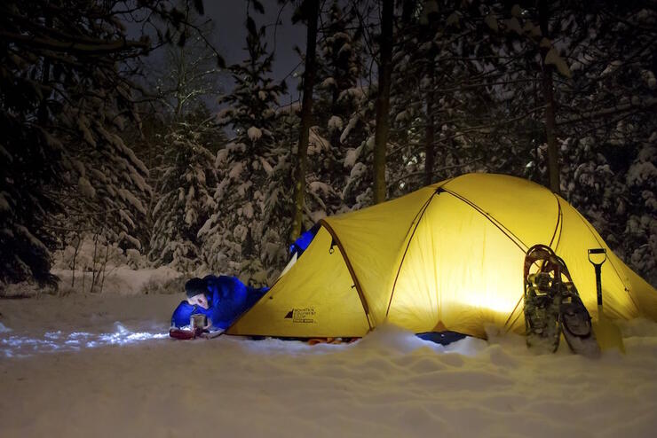 Tent set up in snow with man reading a book. 