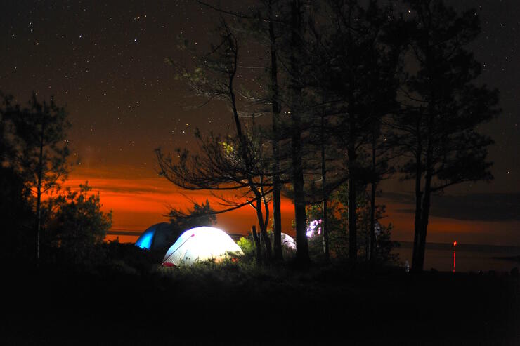 Backlit tent at sunset, nestled under some trees.