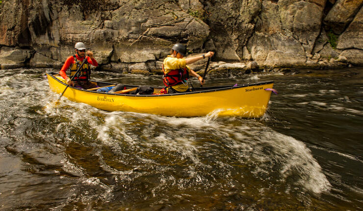 Two canoeists paddling a yellow canoe in whitewater 