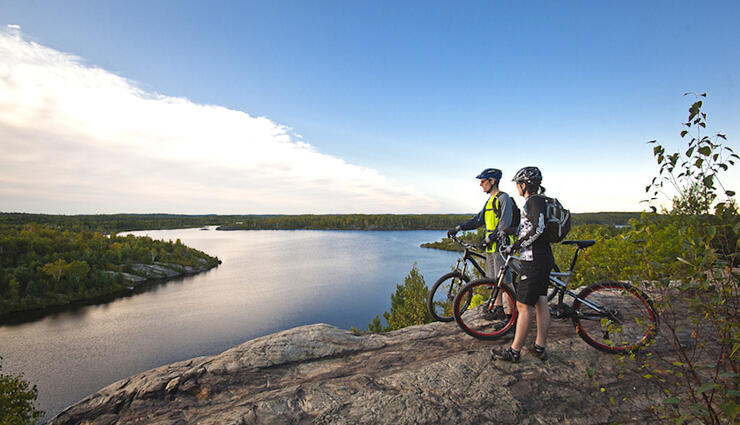 A couple with mountain bikes looking at beautiful view of a lake from top of a cliff