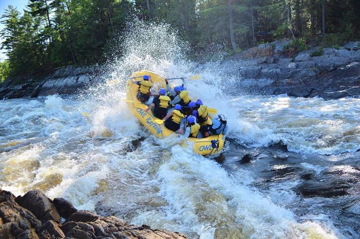 Large raft with people paddling through big rapids. 