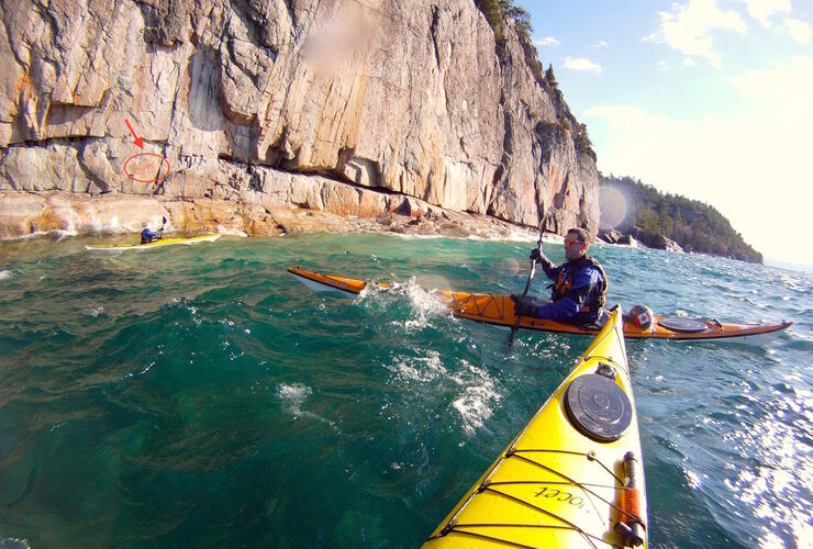 Kayaks paddling in waves, trying to view pictographs. 