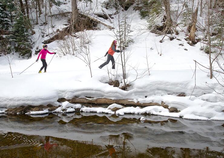 Two women skiing beside an open creek.