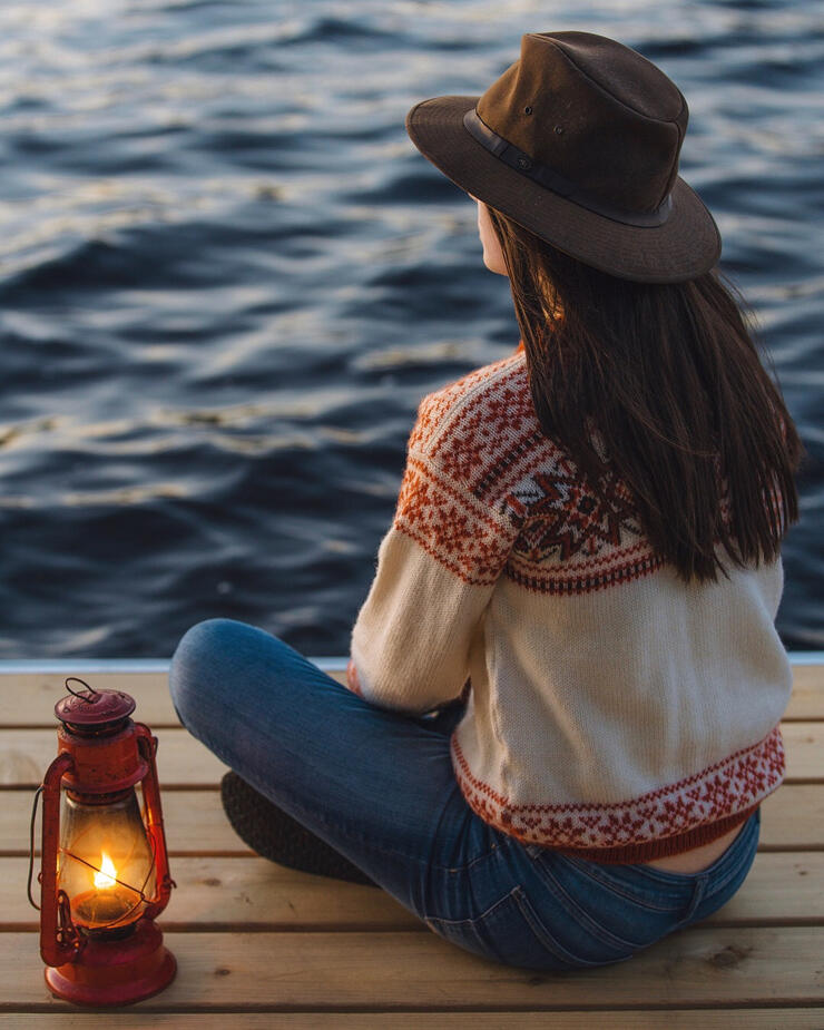 Young woman  with a brimmed hat sitting on a dock beside an old-fashioned lantern.
