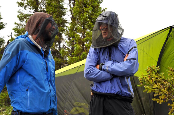 Two men in bug jackets talking in front of a tent. 