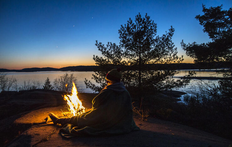Person sitting at campfire at sunset.