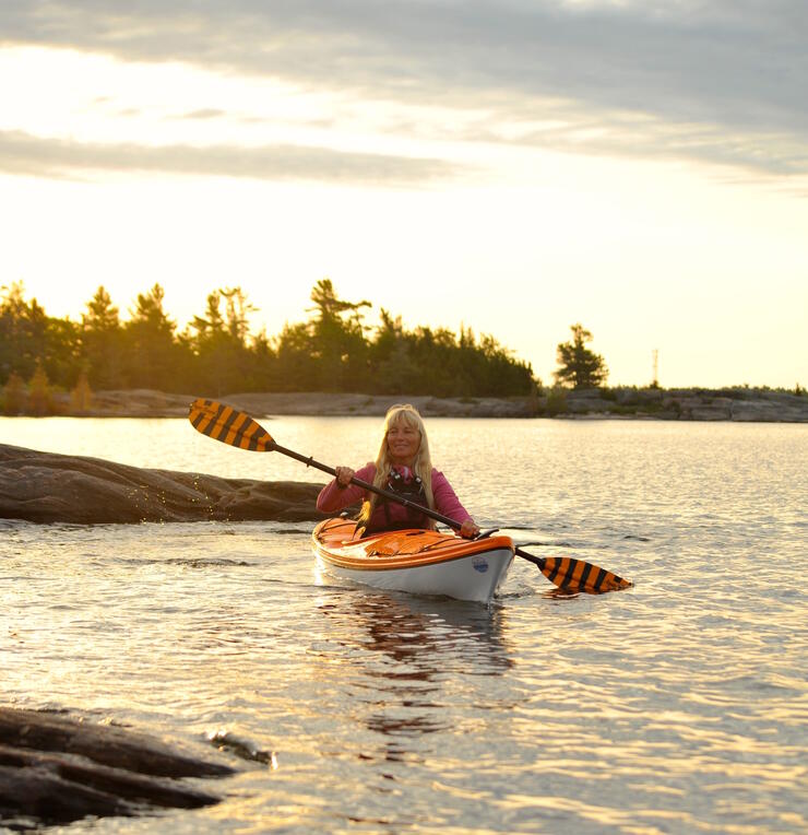 Woman paddling a yellow and white kayak a sunset. 