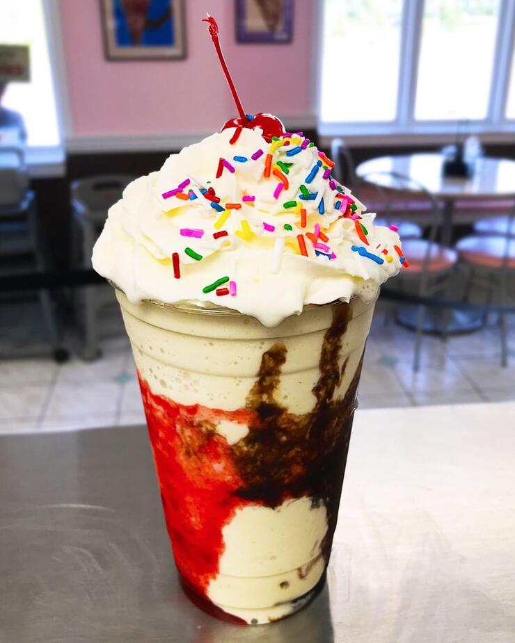 Close up of ice cream sundae with chocolate and strawberry sauce, covered in whipped cream and sprinkles.