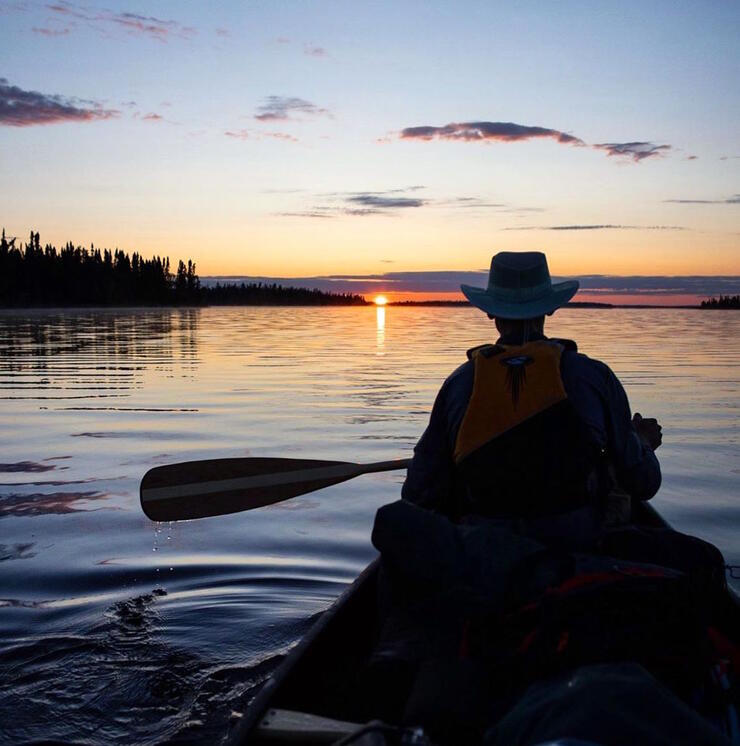 Man paddling in bow of canoe at sunset.