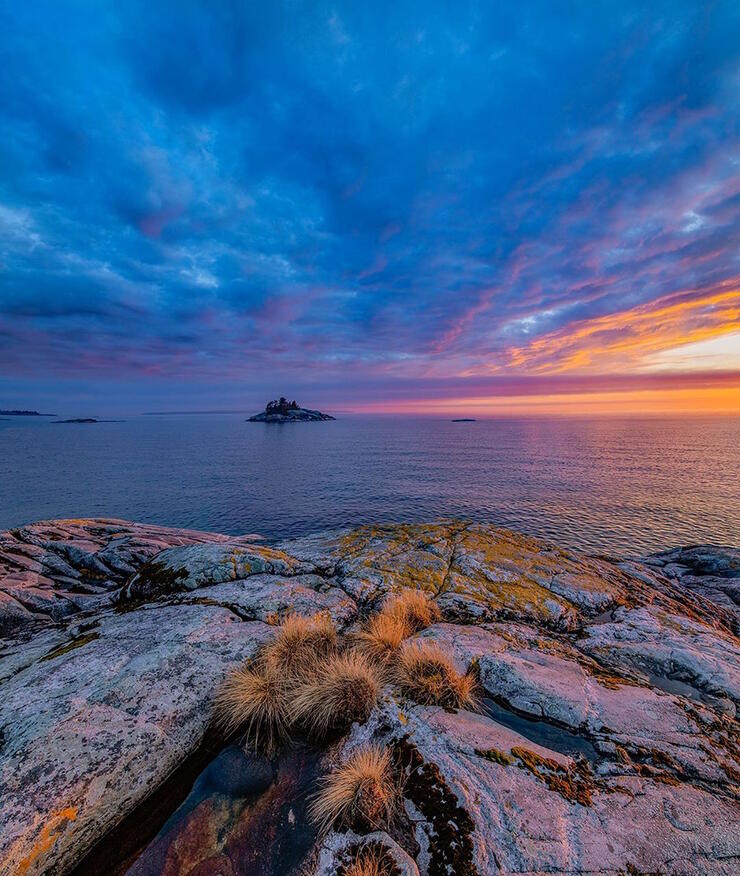 Colourful sunset over Lake Superior with smooth rocks in foreground.
