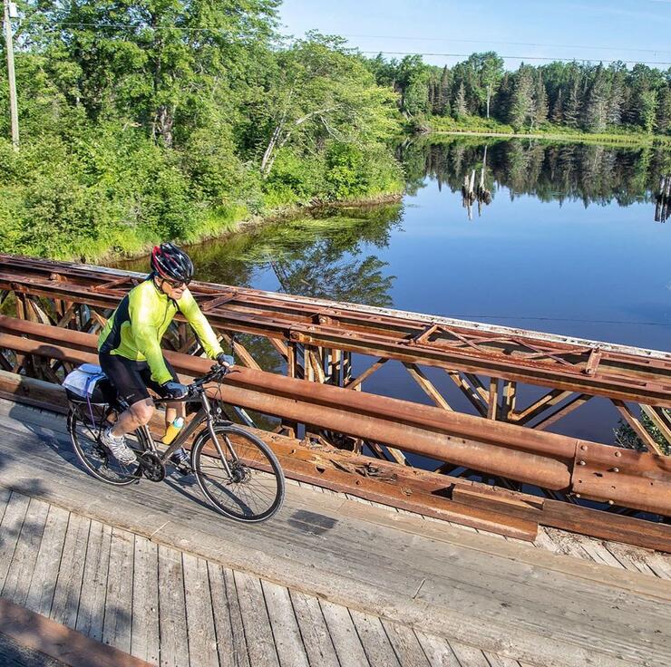Man riding a bicycle on a bridge, over a river.