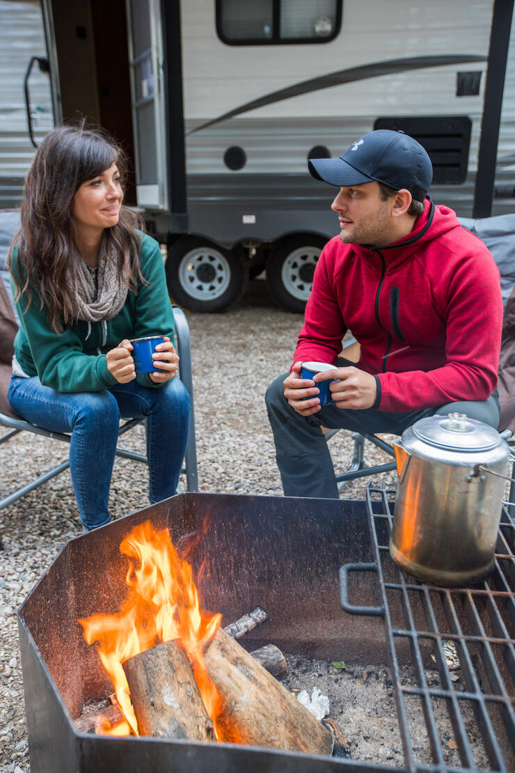 Couple sitting on chairs beside a campfire. 