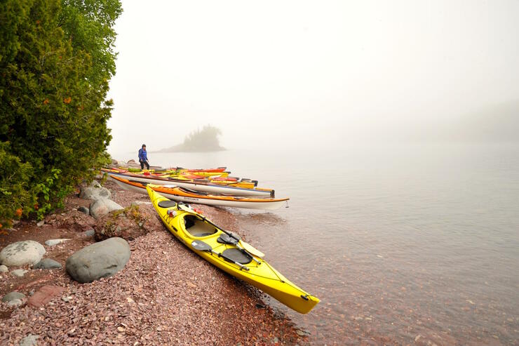 Group of empty kayaks on shore of Lake Superior, covered in by fog.