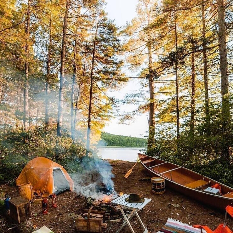 Well organized campsite with a tent, campfire, table, chairs and canoe.