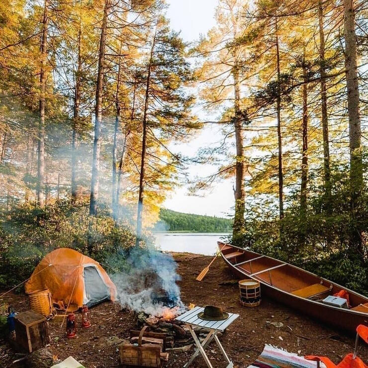 Well organized campsite with a tent, campfire, table, chairs and canoe. 