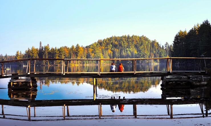 Couple sitting on a small bridge over a calm lake.