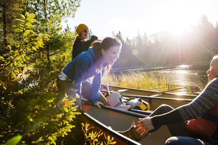 Laughing woman pushing a canoe out from a portage landing.