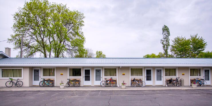 Seven bicycles leaning against benches outside of motel rooms