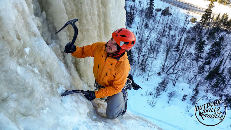 Man with ice picks climbing a frozen waterfall.
