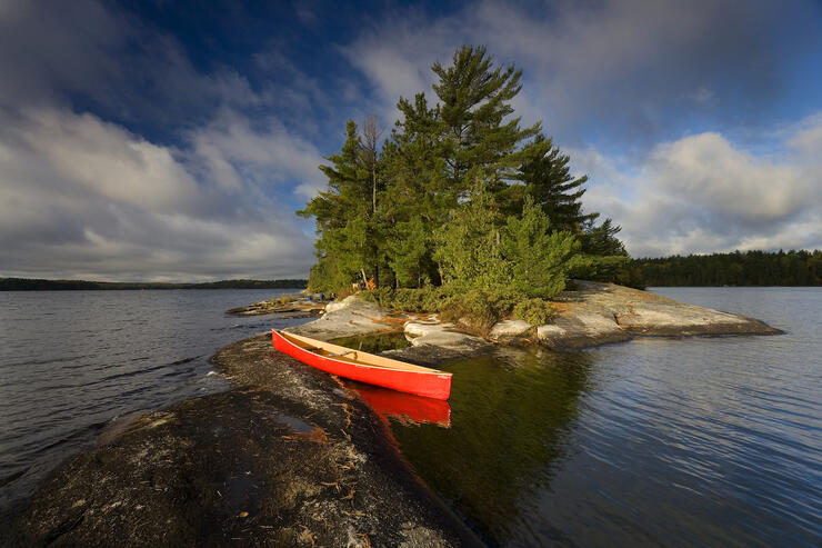 Red canoe beside a small rock island on peaceful lake.