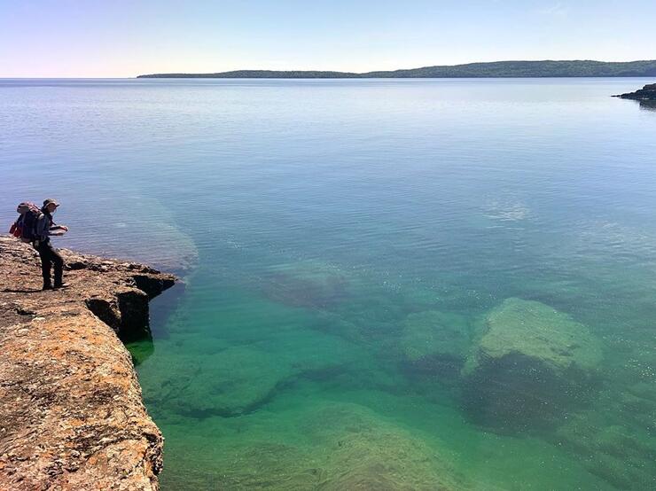 Backpacker standing on a rock shoreline looking out to Lake Superior.