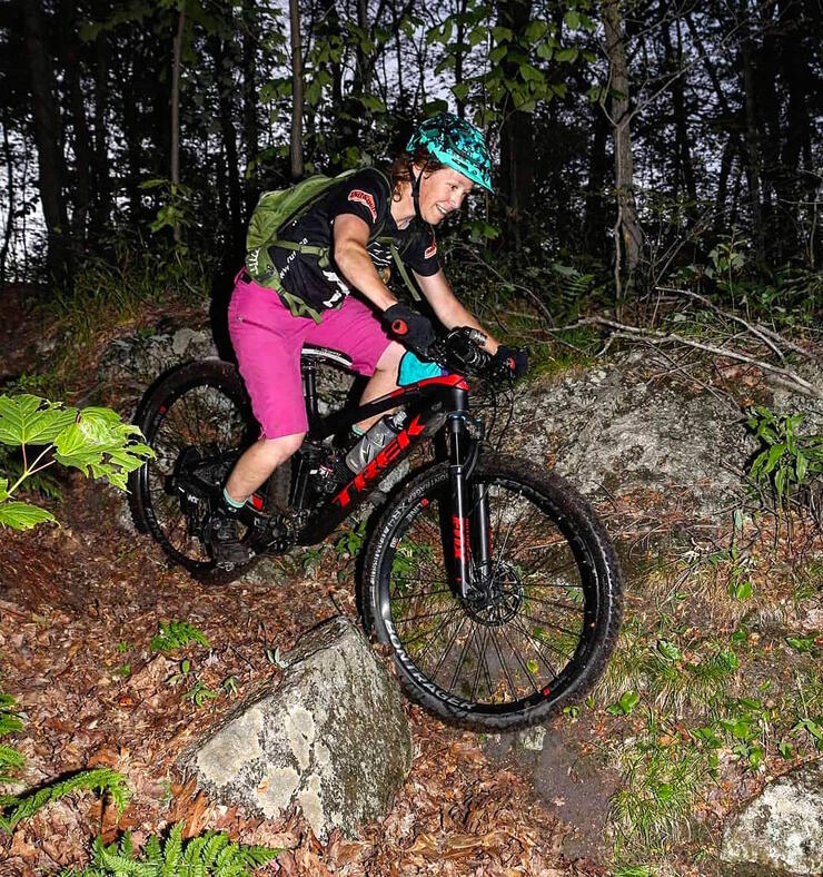 Woman mountain biking over rocks on forest trail.